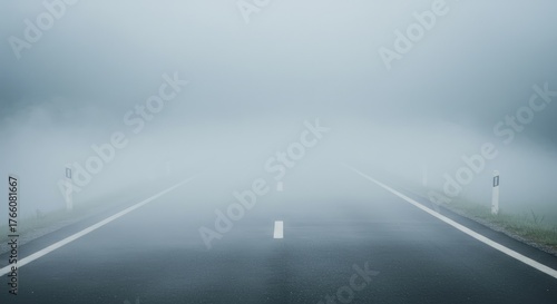 A long, asphalt road disappears into thick fog, flanked by white guide posts. Overcast sky blends with the hazy atmosphere