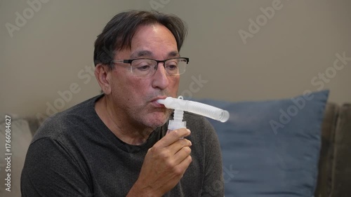 A view of a man using an at-home nebulizer machine to help with breathing and lung recovery after respiratory infection. 14921  	