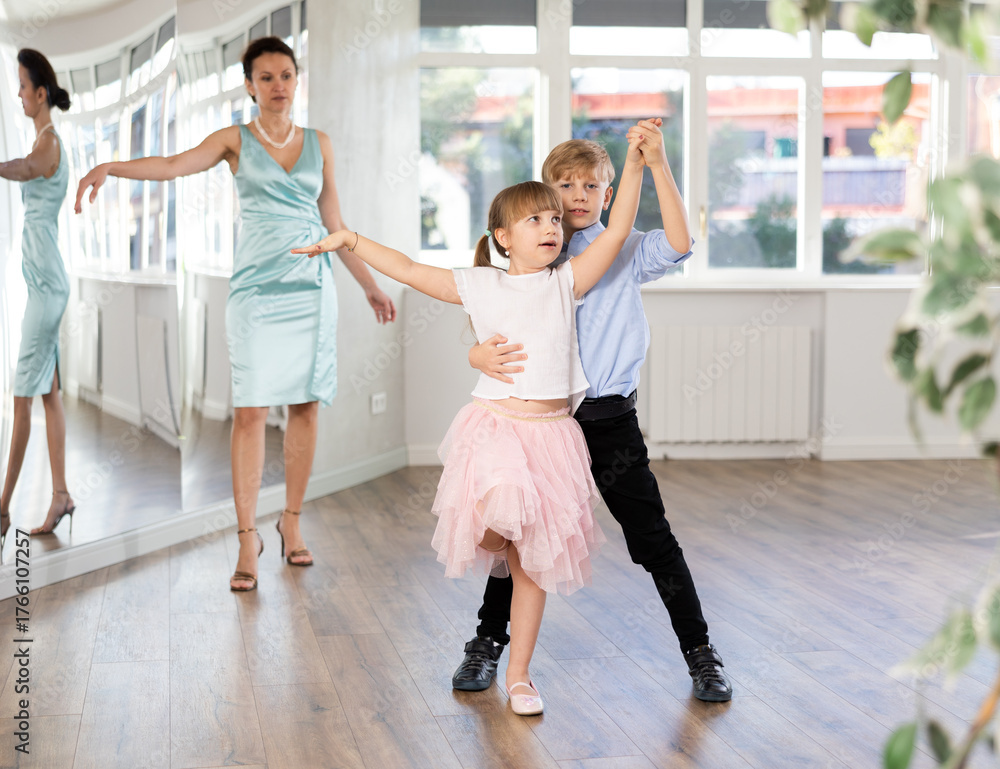 Naklejka premium Boy with girl during contemporary vigorous dancing lesson. Children rehearse rumba movement. Female teacher conducts class for students during dance workout