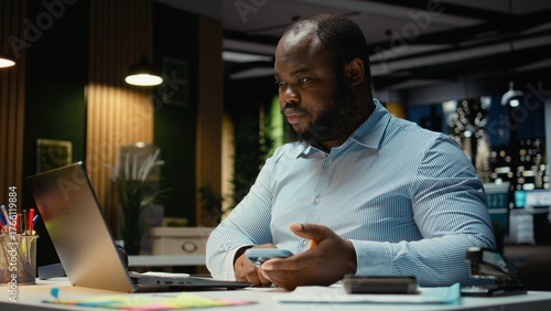 Overworked male worker checking calendar before scheduling engagement, picking up his smartphone to answer texts and read notifications. Person getting distracted and frowning.