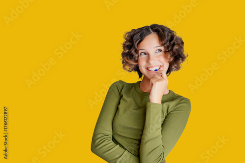 Headshot of laughing cheerful girl with curly hairstyle wearing olive green jumper white toothy smile isolated on bright yellow color background