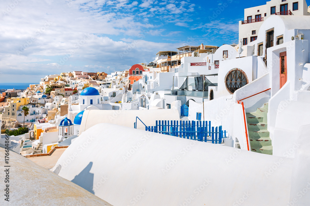 Obraz premium Whitewashed terraces and blue dome churches highlight the colorful townscape of Oia Village, Greece, on the volcanic island of Santorini.