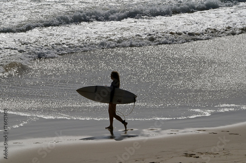 Aerial view of unrecognizable female wave surfer holding a surfing board walking into the sea
