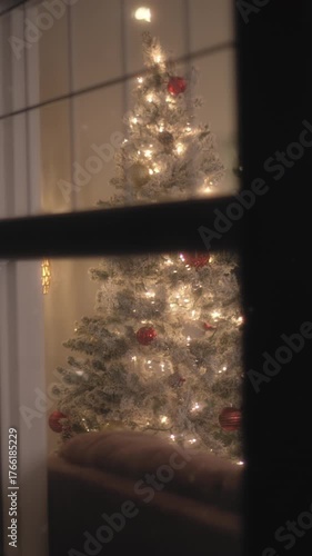 Christmas tree at home with snow falling outside, window view. Vertical format