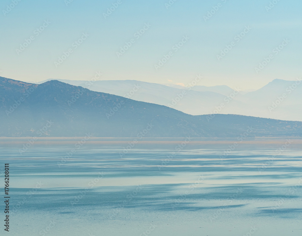 Obraz premium A stunning landscape of a calm turquoise lake with layers of misty blue mountains fading into the horizon a serene and beautiful nature view