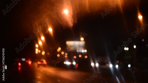 Water drops on the windshield of a car, inside the car when it rains on a city street. Blurred background, red and orange bokeh, Blurred lights outside window when it rains at night