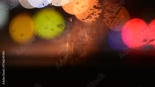 Water drops on the windshield of a car, inside the car when it rains on a city street. Blurred background, red and orange bokeh, Blurred lights outside window when it rains at night