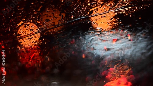 Water drops on the windshield of a car, inside the car when it rains on a city street. Blurred background, red and orange bokeh, Blurred lights outside window when it rains at night