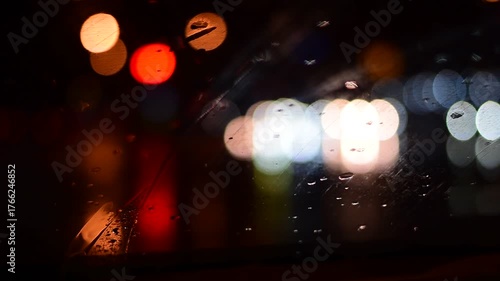 Water drops on the windshield of a car, inside the car when it rains on a city street. Blurred background, red and orange bokeh, Blurred lights outside window when it rains at night