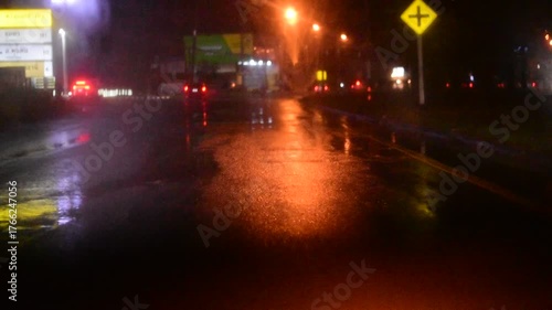 Water drops on the windshield of a car, inside the car when it rains on a city street. Blurred background, red and orange bokeh, Blurred lights outside window when it rains at night