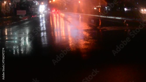 Water drops on the windshield of a car, inside the car when it rains on a city street. Blurred background, red and orange bokeh, Blurred lights outside window when it rains at night