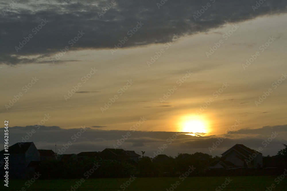 Obraz premium a golden sun shines behind a cloudy sky, below a dark gray cloud, sunrise over a mountain, sunset over the mountains
