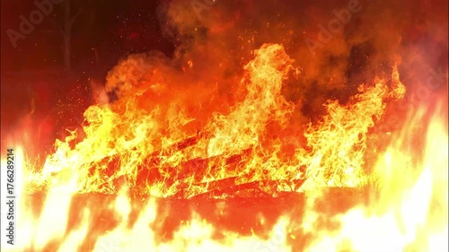 Intense, roaring flames in vibrant orange and yellow engulf the frame, with thick, dark smoke rising against a fiery red background.