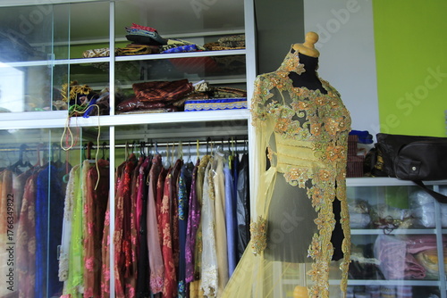Transparent kebaya dress with brocade and beaded ornaments displayed on a mannequin.