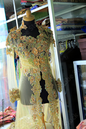 Transparent kebaya dress with brocade and beaded ornaments displayed on a mannequin.