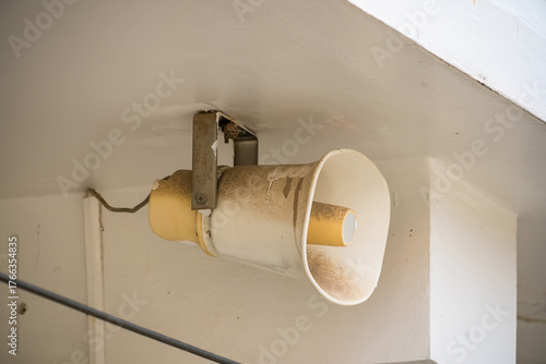 Old dirty white loudspeaker mounted on a ceiling corner of a building used for public announcements or emergency alerts