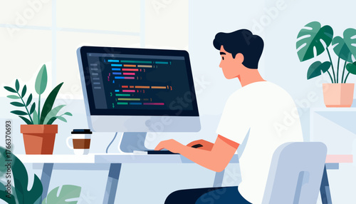 A man is sitting at a desk with a computer monitor in front of him. He is typing on the keyboard and he is focused on his work. The room has a potted plant and a cup on the desk