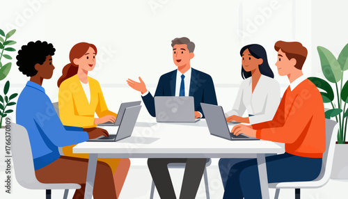 A group of people are sitting around a table with laptops open. The man in the suit is talking to the group. Scene is professional and focused