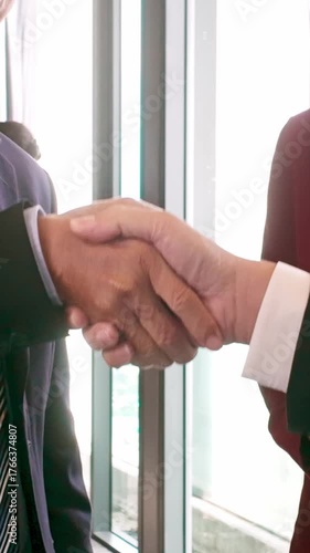 Close-up of two professionals in suits shaking hands near window. Corporate office scene reflects business partnership, contract agreement, deal, negotiation, cooperation, collaboration, and success.