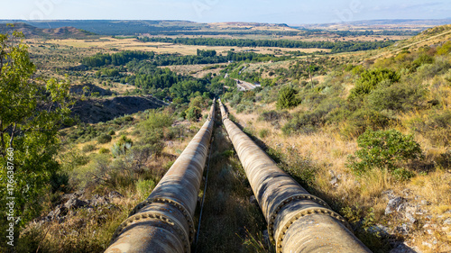 Industrial pipelines crossing a rural valley landscape.