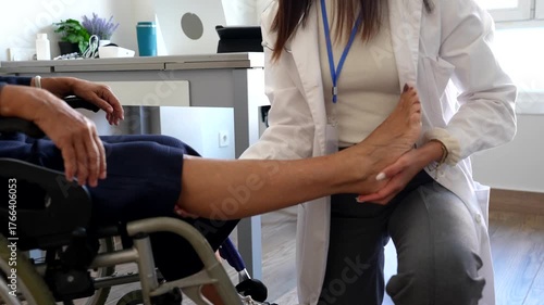 Professional female physiotherapist examining the leg and foot of an elderly woman sitting in a wheelchair, providing specialized rehabilitation and medical assistance in a modern clinic