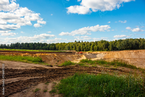 Sprawling sand quarry with heavy machinery extracting material. A vast open pit scene beneath a clear sky and distant green forest