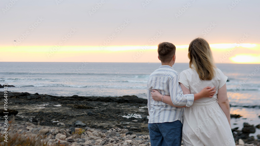 Fototapeta premium A couple delicately embracing each other at sunset on the beautiful beach by the ocean,