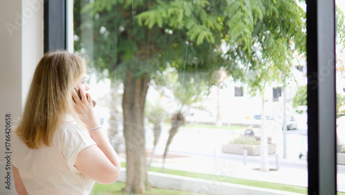Free Download A woman is sitting by the window, talking on the phone and enjoying the beautiful nature outside - GFXLoad