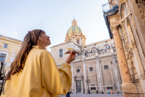 Smiling woman holding a traditional Sicilian cannolo in the historic center of Palermo, Italy. Joyful travel moment and authentic local experience