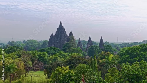 Aerial view of Prambanan Temple emerges from the green canopy, ancient spires piercing the skyline, Yogyakarta, Daerah Istimewa Yogyakarta, Indonesia.