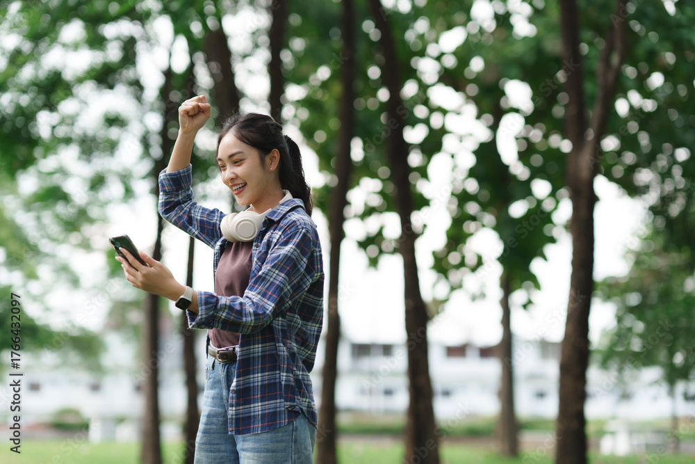 Naklejka premium Young asian woman celebrating success using mobile phone