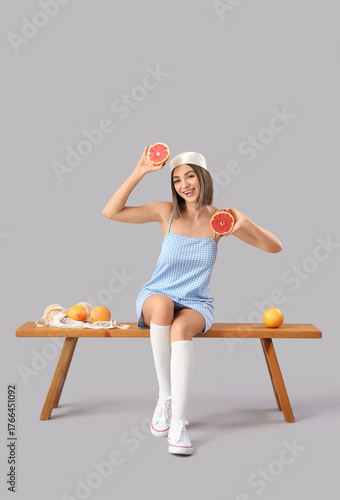 Stylish young woman with grapefruits sitting on bench against light background