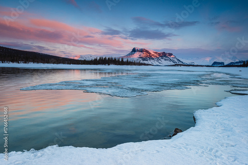 Winter sunrise reveals vibrant colors over frozen lake and snowy peaks at Sarek Nationalpark in Sweden