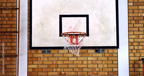 Displaying basketball backboard and rim hanging on brick wall in gym, with net and ladder