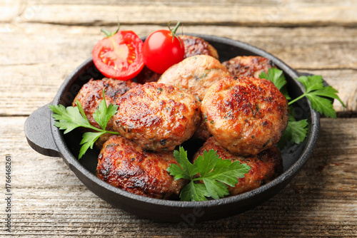 Fotografía Delicious patties with parsley and tomatoes in pan on wooden table, closeup