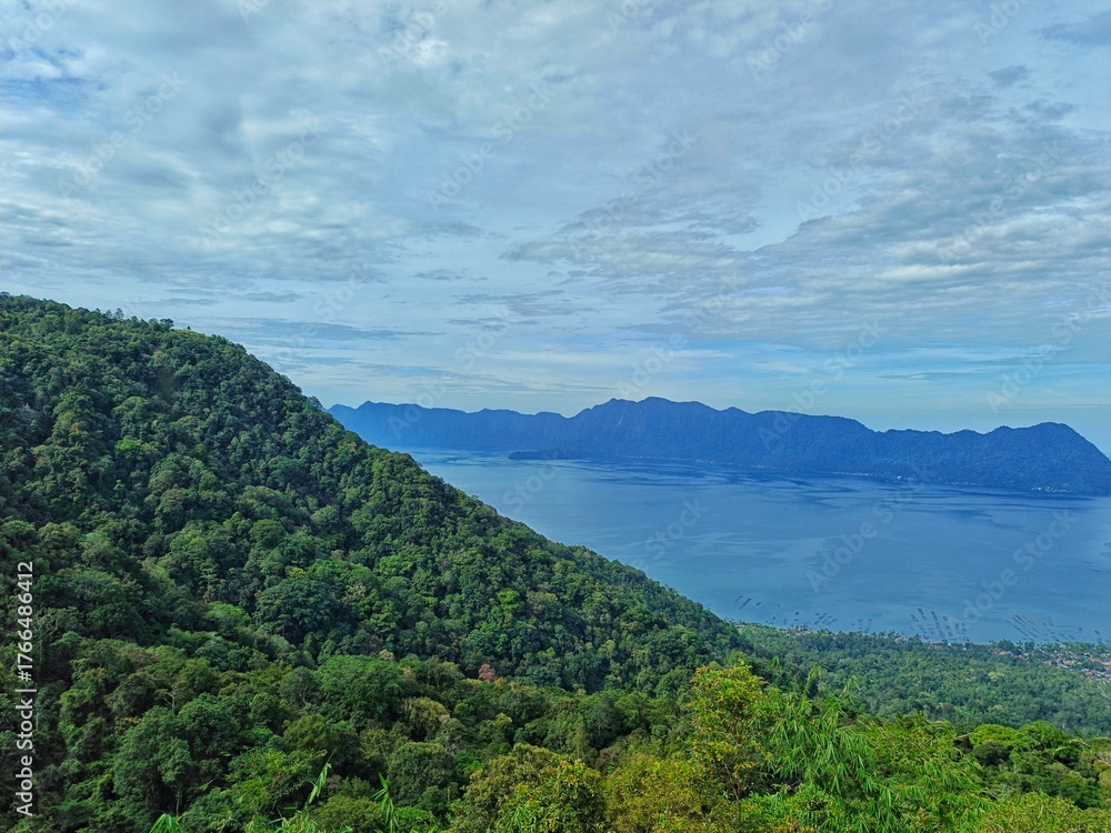 Fototapeta premium Breathtaking Morning View of Lake Maninjau from Puncak Lawang, West Sumatra – Lush Green Hills, Calm Blue Waters, and Distant Mountain Ranges in Indonesia