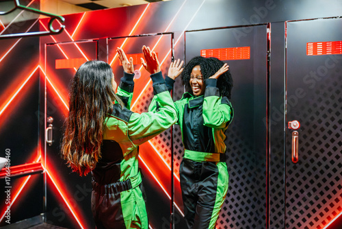 Foto Two women high fiving in racing suits, confidently preparing for a fun go kartin