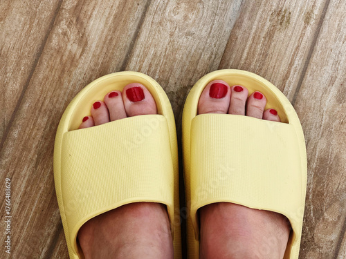 legs with bright red pedicure in yellow slippers on a wooden floor during sunny weather