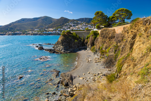 Secluded cove at l’Enbarril beach along the coastal path from Llançà to Port de la Selva, with cliffs, turquoise water, and a hillside village in the background.