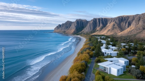 Aerial View of a Rugged Mountainous Coastline Meeting a Sandy Beach with Modern White Buildings Nestled Among Trees Under a Clear Blue Sky