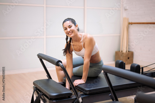 Smiling pilates instructor sitting on reformer in gym after workout