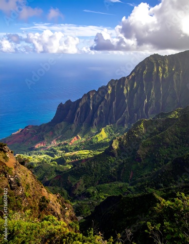 A verdant mountain range meets the vast blue ocean under a partly cloudy sky