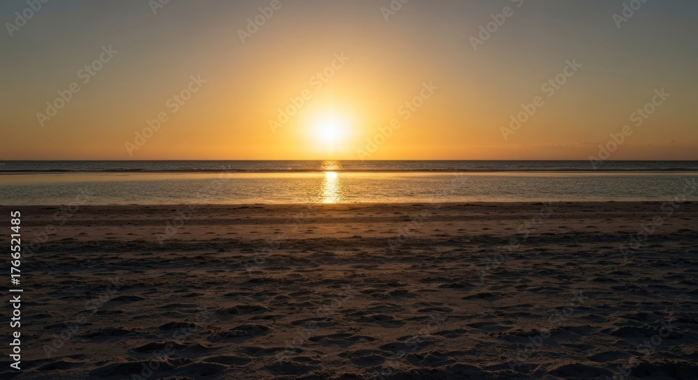 Obraz premium A tranquil beach scene showcases a vibrant sunset over calm waters. Sand in foreground