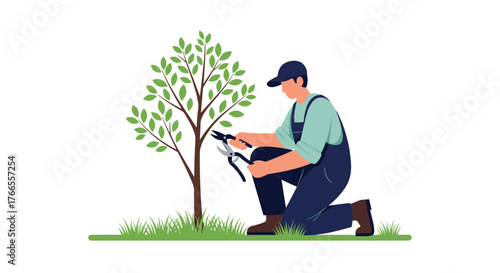 A gardener in overalls and a cap kneels to carefully prune the branches of a young tree with hand shears in a lush green outdoor setting.