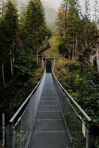 Metal suspension bridge in the Alps near Namlos, Tyrol – hiking trail through dense mountain forest across a deep gorge