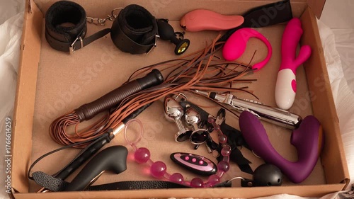 Woman in black transparent glove takes adult toys. BDSM erotic set. Butt plug, gag, handcuffs, whip, nipple clamps, electric stimulator, vibrator