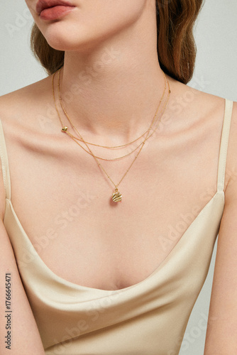 Close-up of a woman wearing layered gold necklaces and a beige satin top.