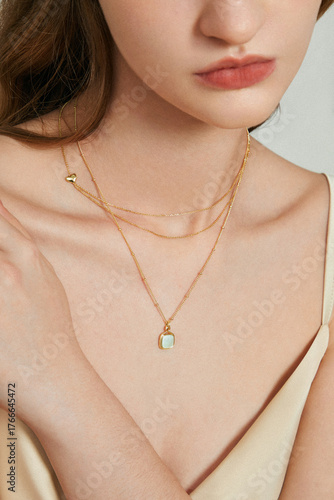 Close-up portrait of a woman wearing layered gold necklaces and a delicate silk top.