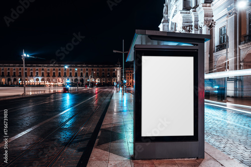 Night city scene with illuminated blank billboard mockup at a modern bus stop, wet pavement reflecting neon lights and passing traffic, perfect for urban advertising or branding presentation
