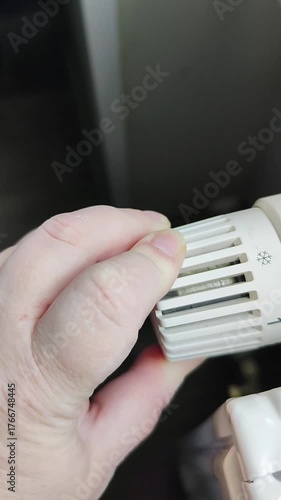 Hand adjusting temperature control on a radiator, showcasing gradual movement and focus on the dial, emphasizing warmth and comfort in the environment